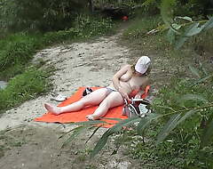 Wild beach. Random passerby cadger squeaks on sunbathing go-go beautiful Mummy on the river bank Outdoors. Outside. Naked in